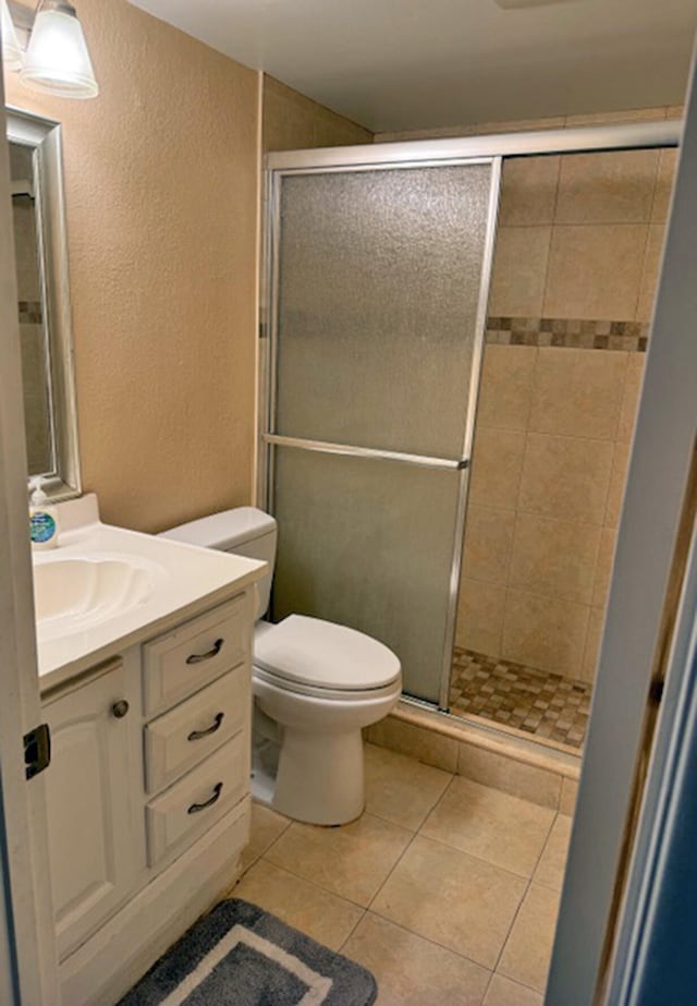 bathroom with toilet, vanity, tile patterned floors, and a shower with shower door