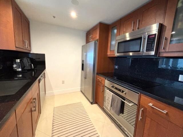 kitchen featuring dark stone counters, backsplash, light tile patterned floors, and stainless steel appliances