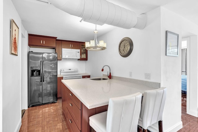 kitchen featuring pendant lighting, kitchen peninsula, sink, white appliances, and a kitchen breakfast bar