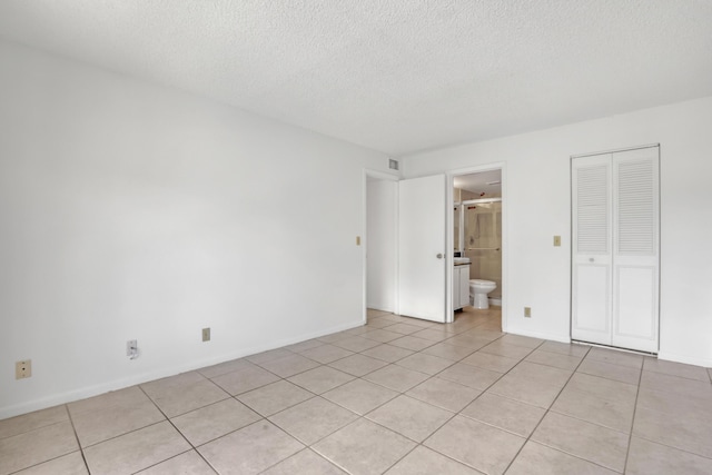 unfurnished bedroom with light tile patterned floors, a textured ceiling, ensuite bathroom, and a closet