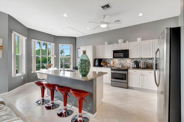 kitchen featuring a center island with sink, light stone countertops, a kitchen bar, white cabinetry, and stainless steel appliances