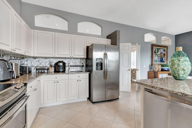 kitchen featuring stove, stainless steel refrigerator with ice dispenser, light tile patterned floors, light stone counters, and white cabinetry