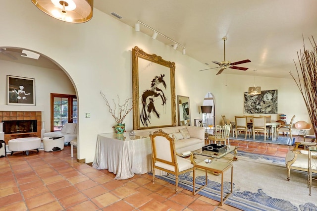 tiled living room with ceiling fan, a fireplace, rail lighting, and high vaulted ceiling