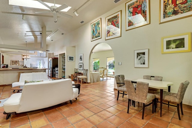 tiled living room featuring a textured ceiling, a towering ceiling, ceiling fan with notable chandelier, and track lighting