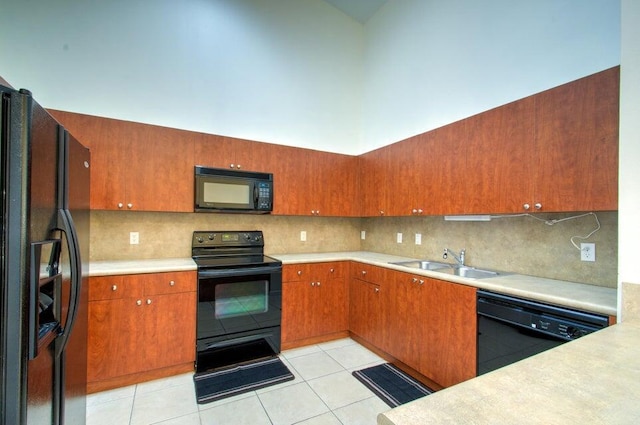 kitchen with sink, black appliances, light tile patterned floors, decorative backsplash, and a high ceiling