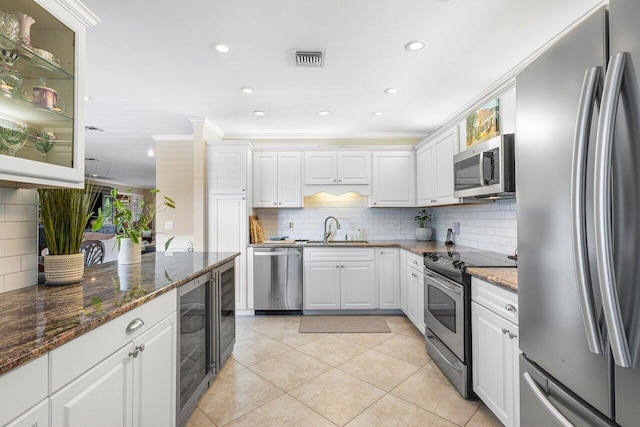 kitchen with stainless steel appliances, crown molding, white cabinetry, dark stone countertops, and wine cooler