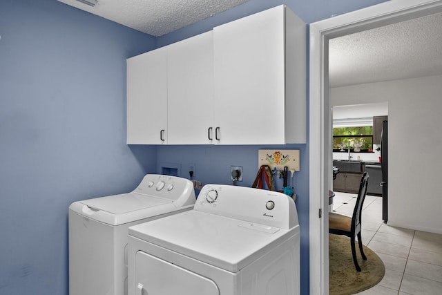 clothes washing area featuring cabinets, light tile patterned floors, washing machine and clothes dryer, and a textured ceiling