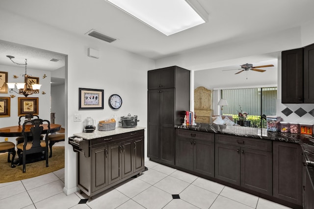 kitchen with light tile patterned floors, hanging light fixtures, dark brown cabinets, ceiling fan with notable chandelier, and dark stone counters