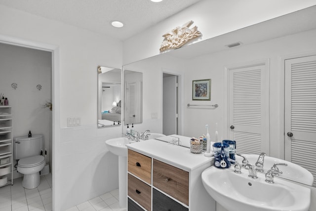 bathroom with double sink, tile patterned floors, toilet, and a textured ceiling