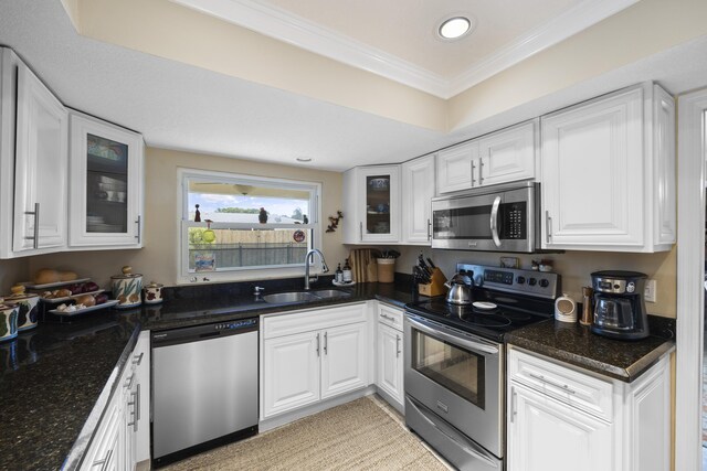 kitchen with sink, white cabinetry, dark stone countertops, ornamental molding, and stainless steel appliances