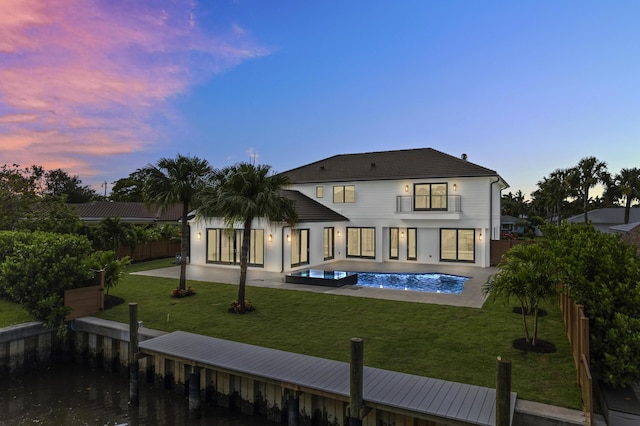 back house at dusk featuring a fenced in pool, a patio, a balcony, and a yard