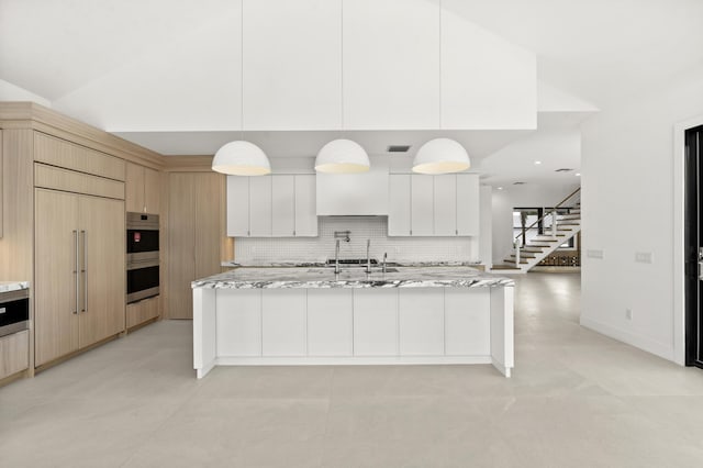 kitchen featuring pendant lighting, light brown cabinets, a center island with sink, paneled built in fridge, and white cabinetry