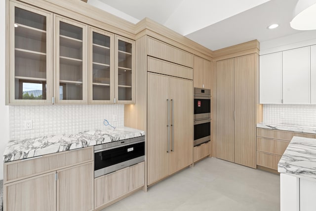 kitchen with light brown cabinets, paneled built in refrigerator, tasteful backsplash, light stone counters, and stainless steel double oven