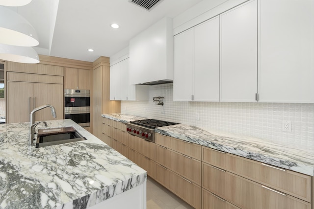 kitchen featuring light stone countertops, white cabinetry, sink, appliances with stainless steel finishes, and custom exhaust hood