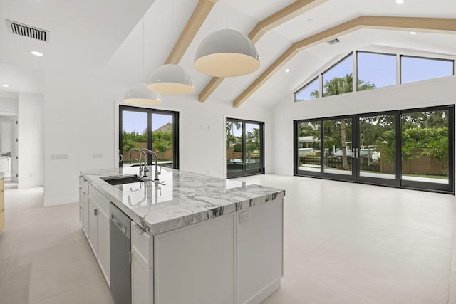 kitchen featuring white cabinetry, sink, hanging light fixtures, light stone counters, and an island with sink