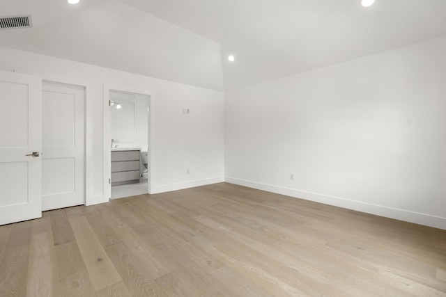 unfurnished bedroom featuring connected bathroom, light hardwood / wood-style flooring, and vaulted ceiling