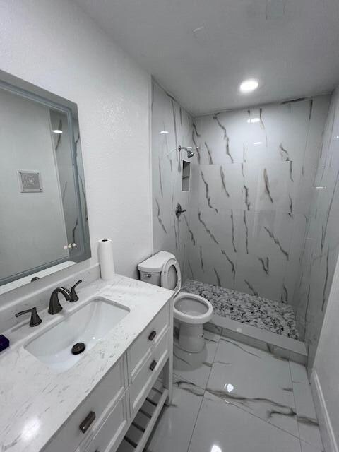 bathroom featuring vanity, toilet, tile patterned floors, and a tile shower