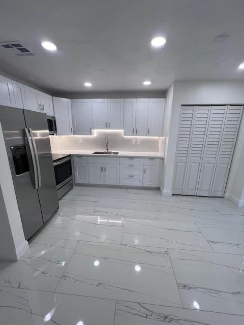 kitchen featuring sink, appliances with stainless steel finishes, white cabinetry, and light tile patterned floors