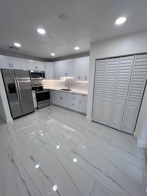 kitchen with sink, appliances with stainless steel finishes, white cabinets, and light tile patterned floors