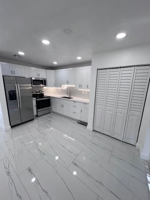 kitchen with sink, appliances with stainless steel finishes, white cabinets, and light tile patterned floors