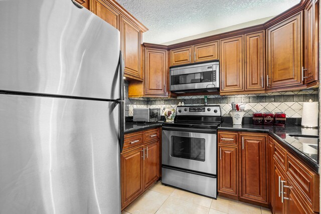 kitchen with dark stone countertops, appliances with stainless steel finishes, tasteful backsplash, a textured ceiling, and light tile patterned floors