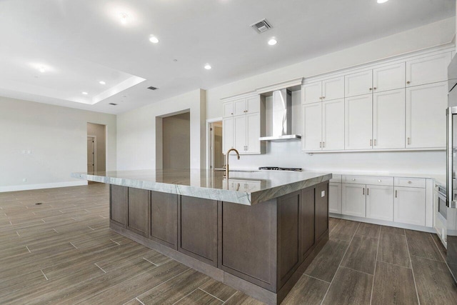 kitchen featuring white cabinets, a spacious island, wall chimney range hood, and stainless steel gas cooktop