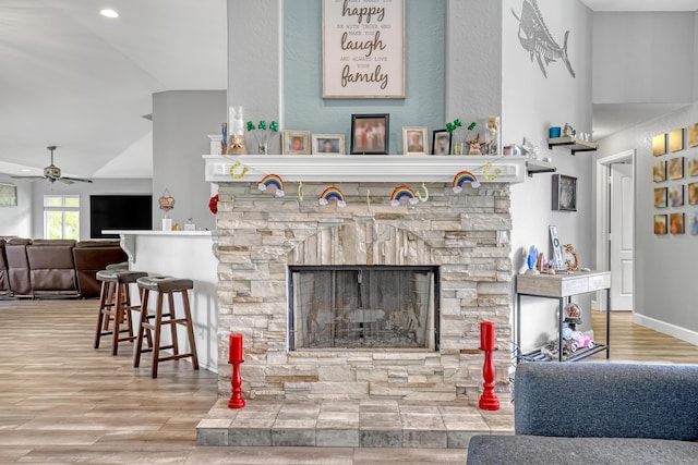 living room with a stone fireplace, ceiling fan, and lofted ceiling