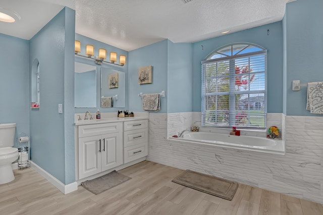 bathroom featuring vanity, a textured ceiling, a relaxing tiled tub, and toilet