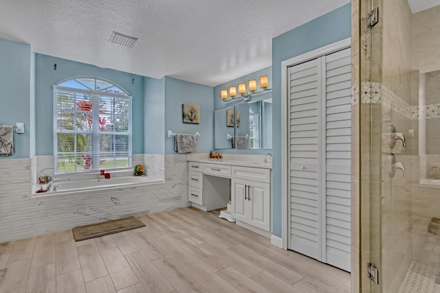 bathroom featuring vanity, a textured ceiling, and plus walk in shower