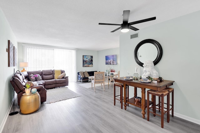 living room featuring ceiling fan, light hardwood / wood-style floors, and a textured ceiling