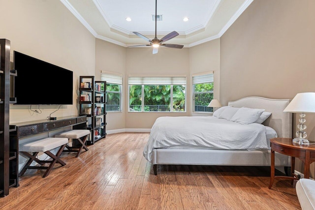 bedroom featuring crown molding, light wood-type flooring, a high ceiling, ceiling fan, and a raised ceiling