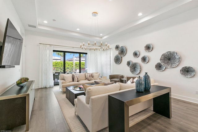 living room featuring an inviting chandelier, hardwood / wood-style flooring, and a raised ceiling