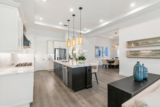 kitchen featuring stainless steel appliances, pendant lighting, an island with sink, a breakfast bar, and light hardwood / wood-style flooring