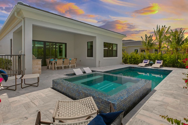 pool at dusk with an in ground hot tub and a patio