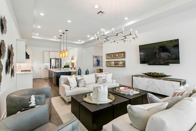 living room with an inviting chandelier, light wood-type flooring, and a tray ceiling