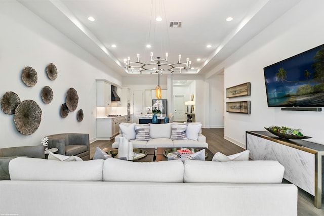 living room featuring a tray ceiling, a notable chandelier, and dark wood-type flooring