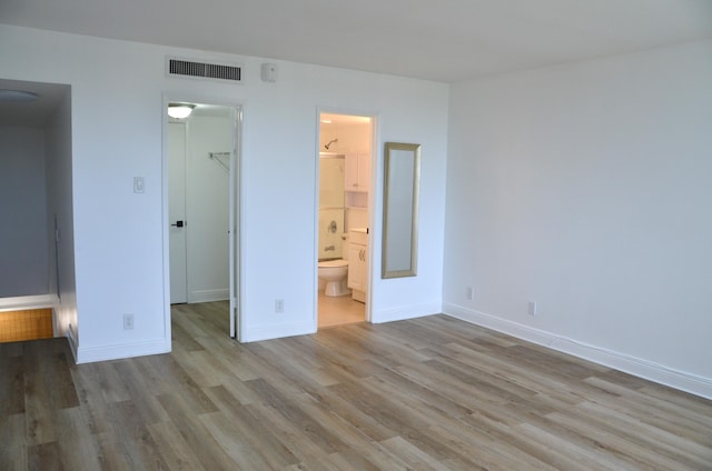 unfurnished bedroom with a walk in closet, ensuite bathroom, a closet, and light wood-type flooring