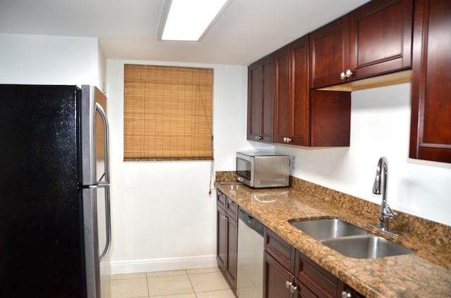 kitchen with sink, light tile patterned floors, stainless steel appliances, and stone countertops