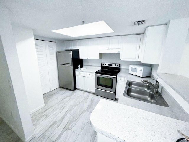 kitchen featuring a skylight, white cabinetry, appliances with stainless steel finishes, sink, and a textured ceiling