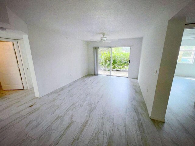 unfurnished room featuring ceiling fan, light hardwood / wood-style floors, a healthy amount of sunlight, and a textured ceiling