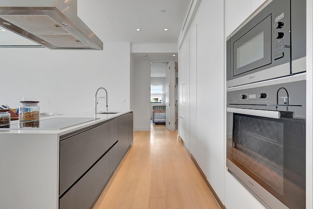 kitchen with white cabinetry, exhaust hood, sink, appliances with stainless steel finishes, and light hardwood / wood-style floors