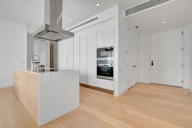 kitchen featuring stainless steel appliances, a kitchen island, island exhaust hood, white cabinets, and light hardwood / wood-style floors