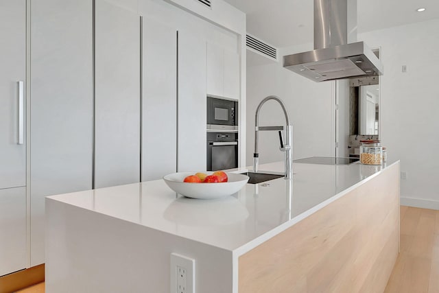 kitchen featuring island range hood, white cabinetry, appliances with stainless steel finishes, and an island with sink