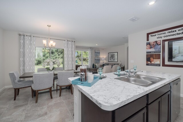 kitchen with an inviting chandelier, sink, hanging light fixtures, stainless steel dishwasher, and an island with sink