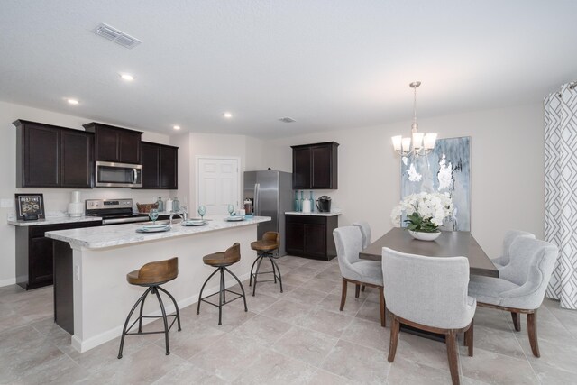 kitchen with hanging light fixtures, stainless steel appliances, an island with sink, a chandelier, and a breakfast bar area