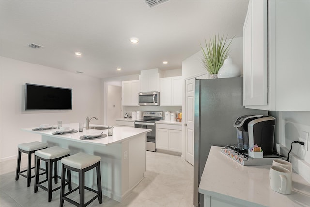 kitchen with stainless steel appliances, an island with sink, and white cabinets