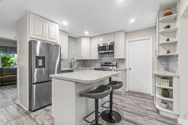 kitchen with appliances with stainless steel finishes, white cabinetry, light hardwood / wood-style flooring, a kitchen island, and a breakfast bar area