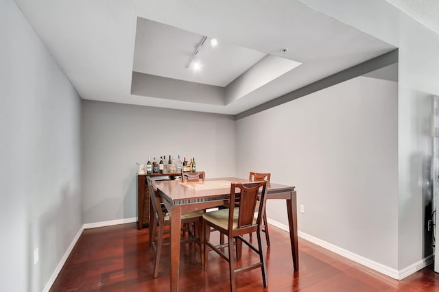 dining area with track lighting, a raised ceiling, baseboards, and wood finished floors