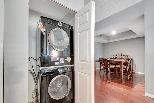 washroom featuring a textured ceiling, laundry area, stacked washer / dryer, wood finished floors, and baseboards