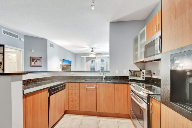 kitchen with appliances with stainless steel finishes, dark stone counters, ceiling fan, sink, and light tile patterned flooring